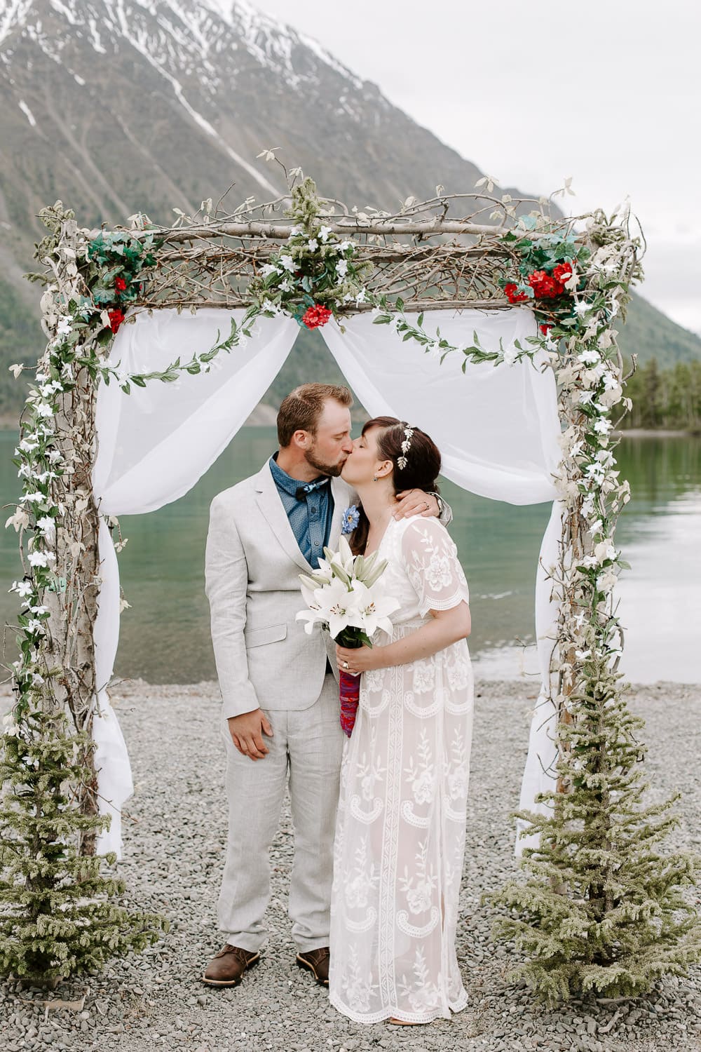 A couple having their first kiss under a flower arch in front of a glacier lake. Destination wedding photographer.