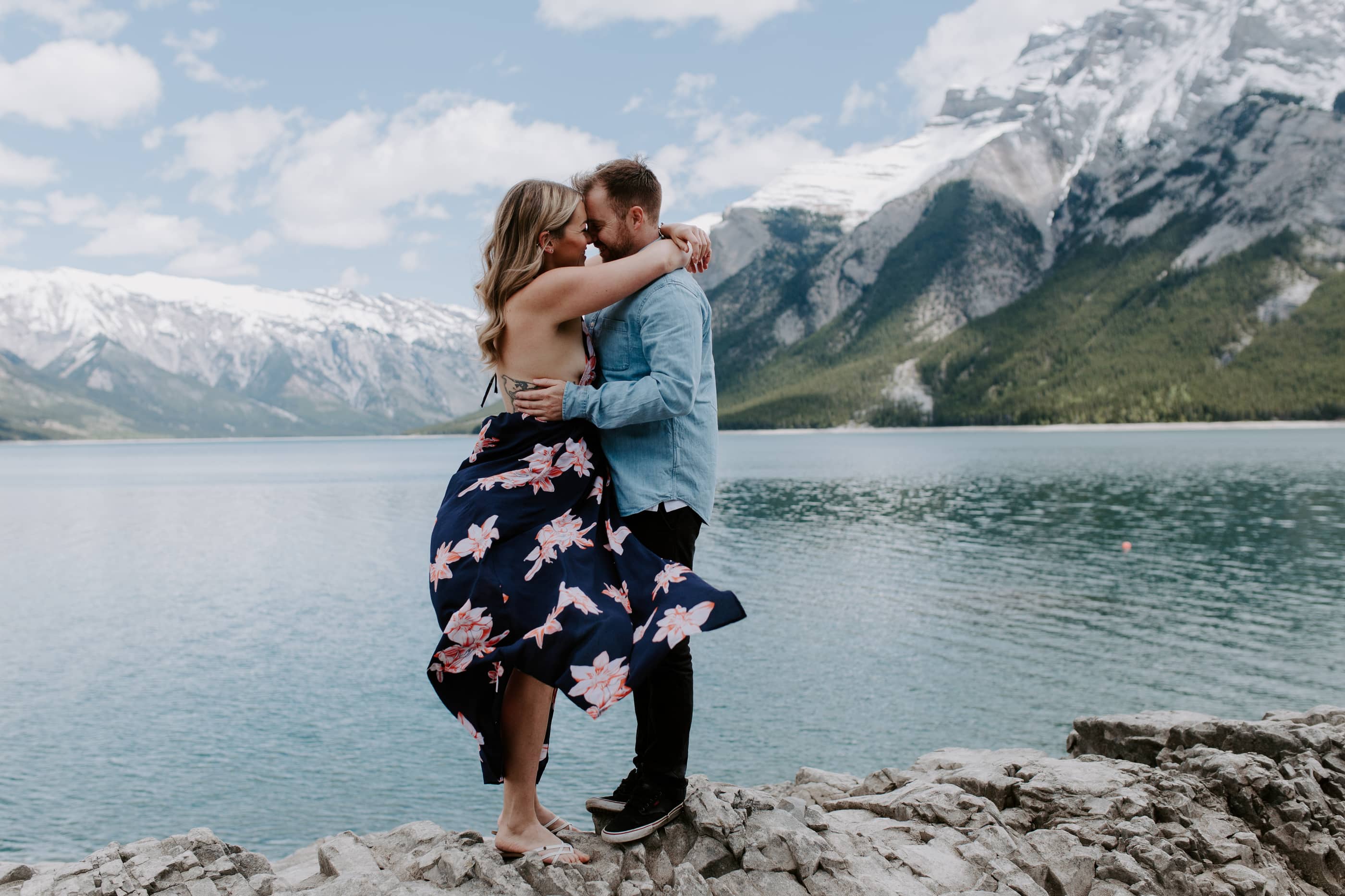 Couple holding each other standing on a rock in front of a lake and mountain range. Kitchener Waterloo Wedding Photographer.