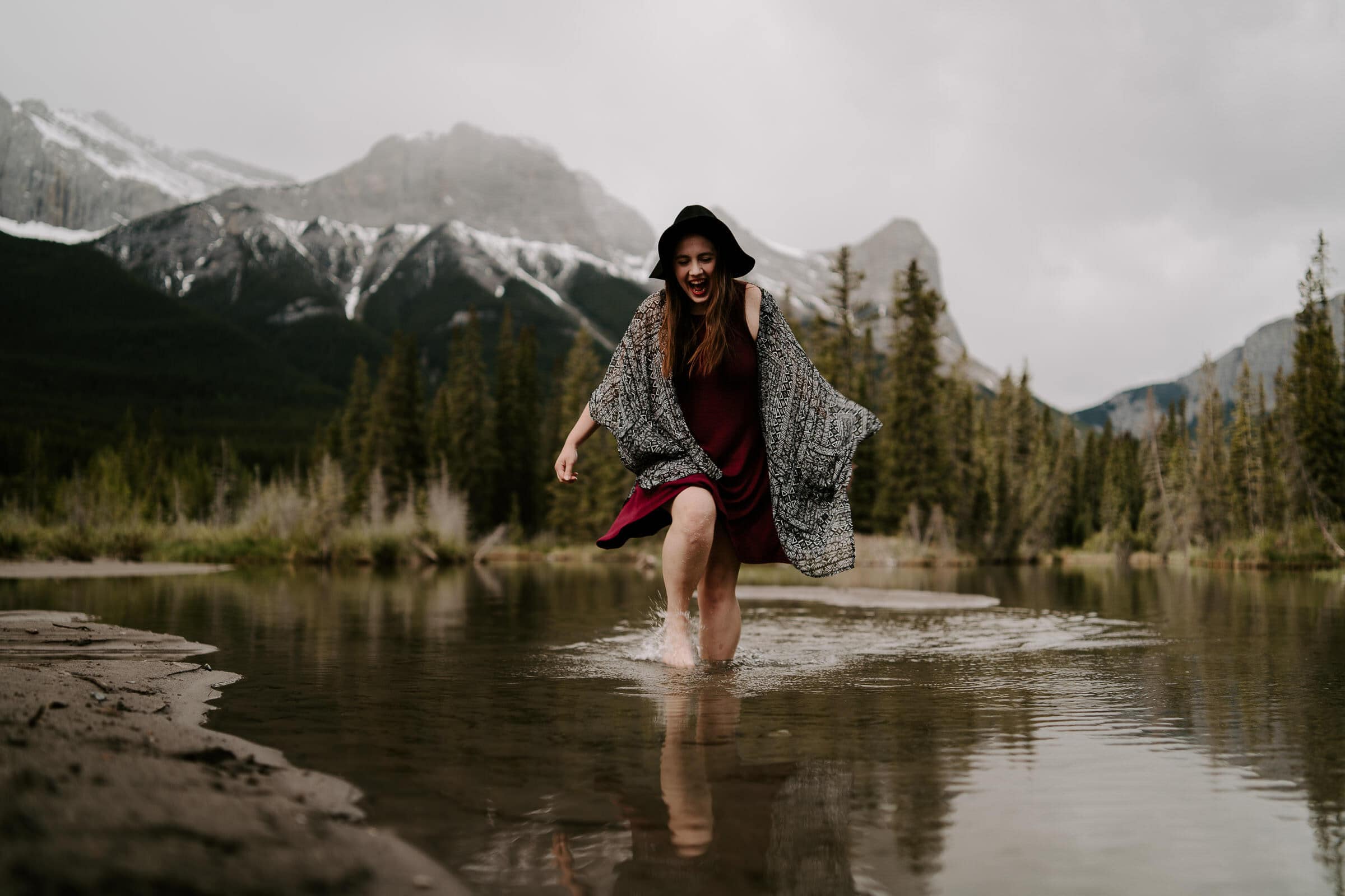 A woman photographer walking through water in front of mountains.