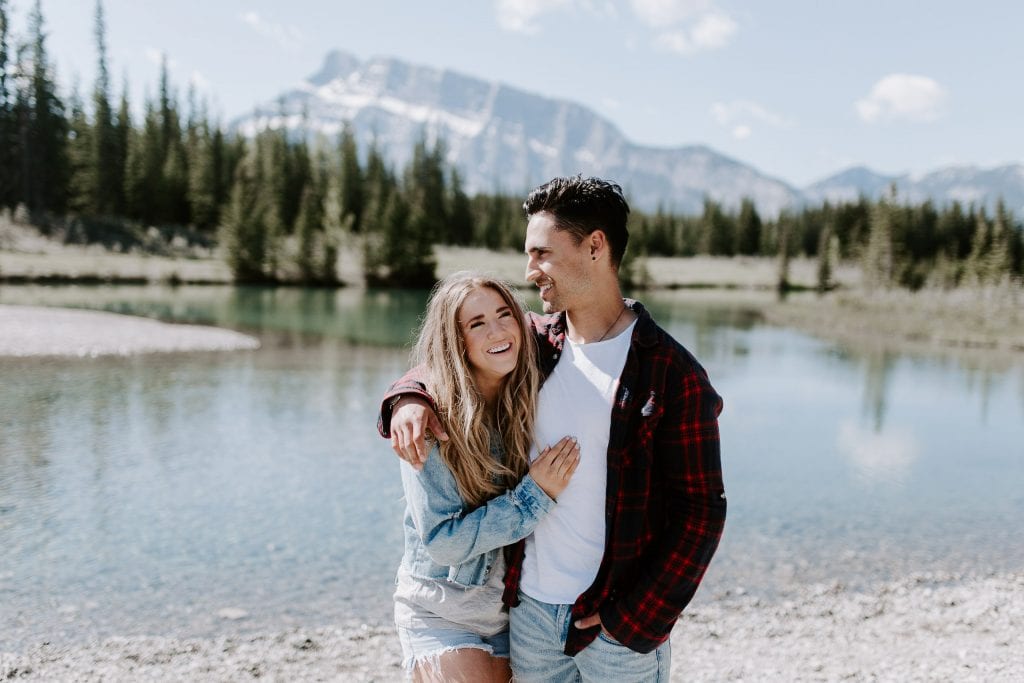 couple laughing and cuddling in front of a pond with mountains in the backgound. Banff elopement photographer