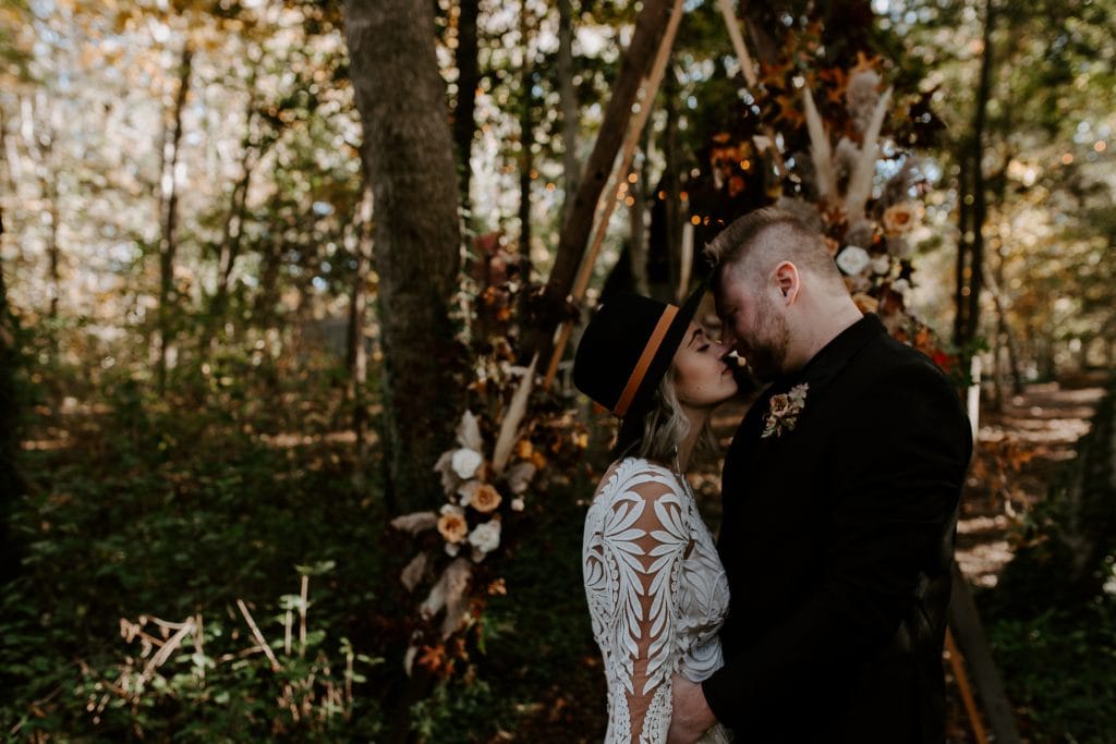 A small wedding couple kissing in front of a flower arch in the woods. Kitchener wedding photographer