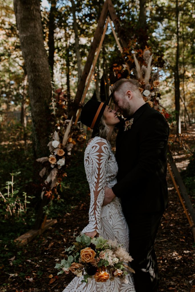 A couple kissing in front of their flower arch on their elopement day at a cabin in the woods. Muskoka Ontario elopement photographer