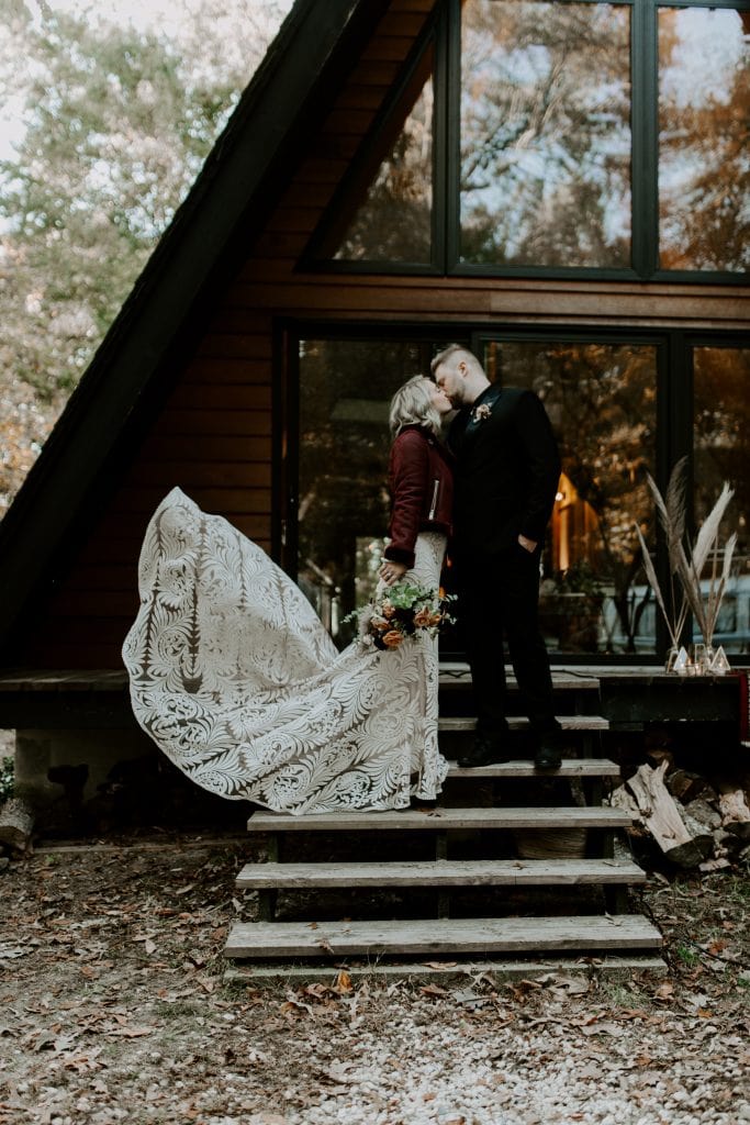 A couple kissing on their elopement day in front of their cabin in the woods. Ontario small wedding and elopement photographer.